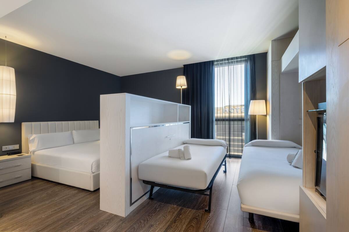 Une chambre d’hôtel avec un lit, un canapé, un bureau et une fenêtre avec des rideaux.