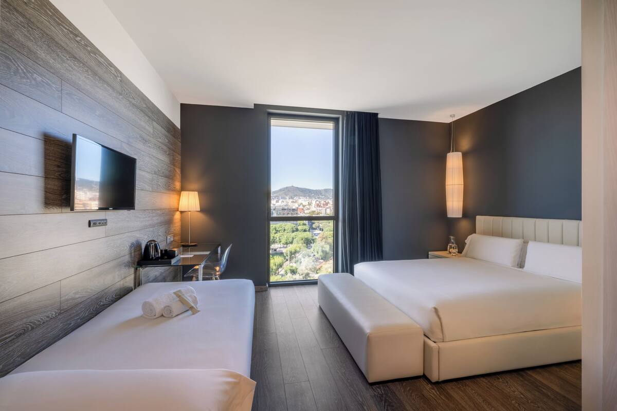 Une chambre d’hôtel avec deux lits, une télévision, un bureau avec une lampe et une vue sur la ville.