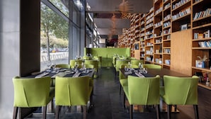 Un restaurant moderne avec des chaises et des tables vertes, de grandes fenêtres et des étagères remplies de livres.