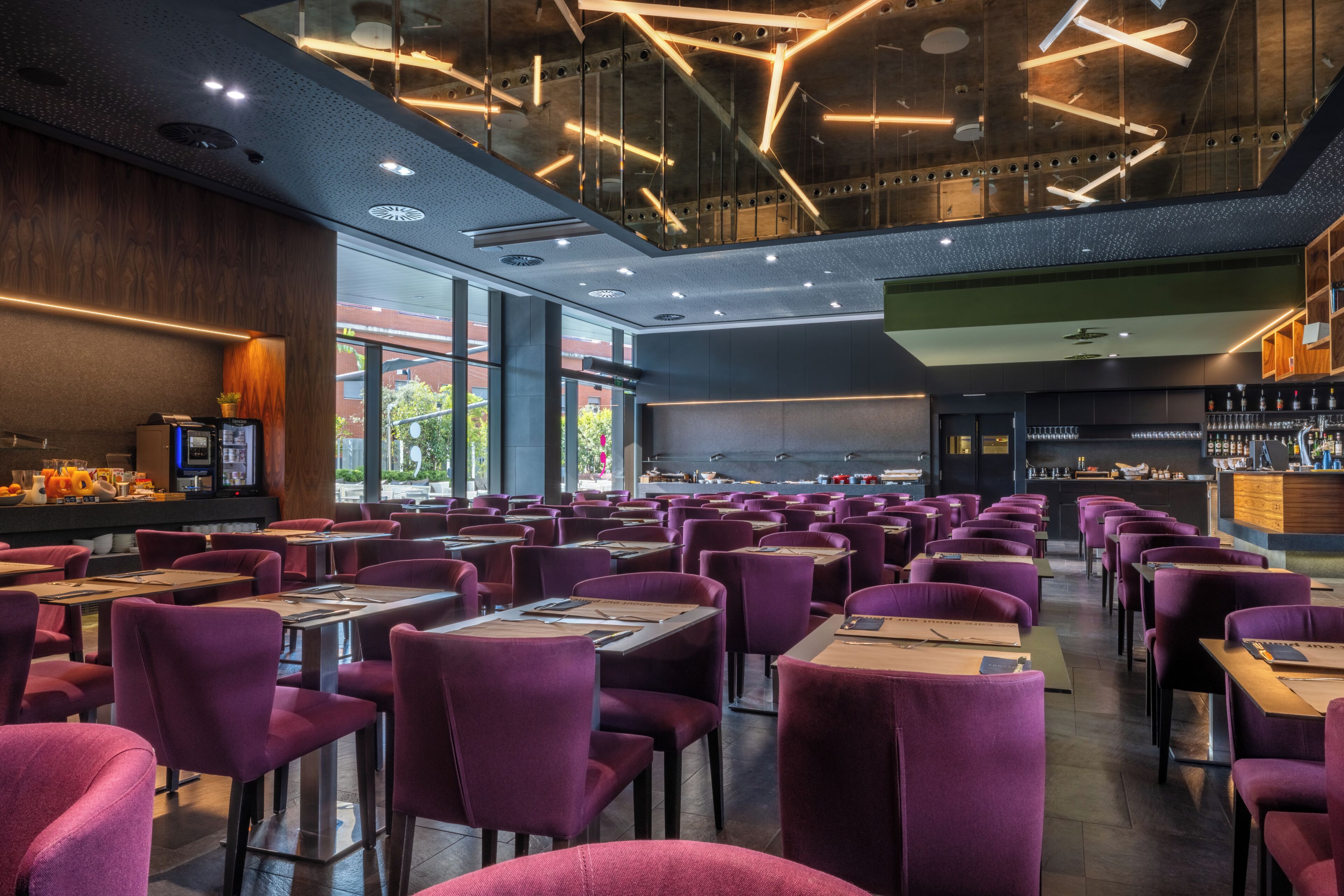 A modern restaurant with purple seating, a bar area, and a large screen.