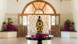 Une pièce avec un mur en pierre, des portes en bois et une table centrale agrémentée d’un vase décoratif et de fleurs.