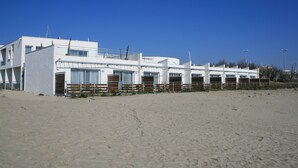 A row of white beachside cottages with multiple windows and a sandy beach in the foreground. - Residence Côté Mer (La Grande-Motte)