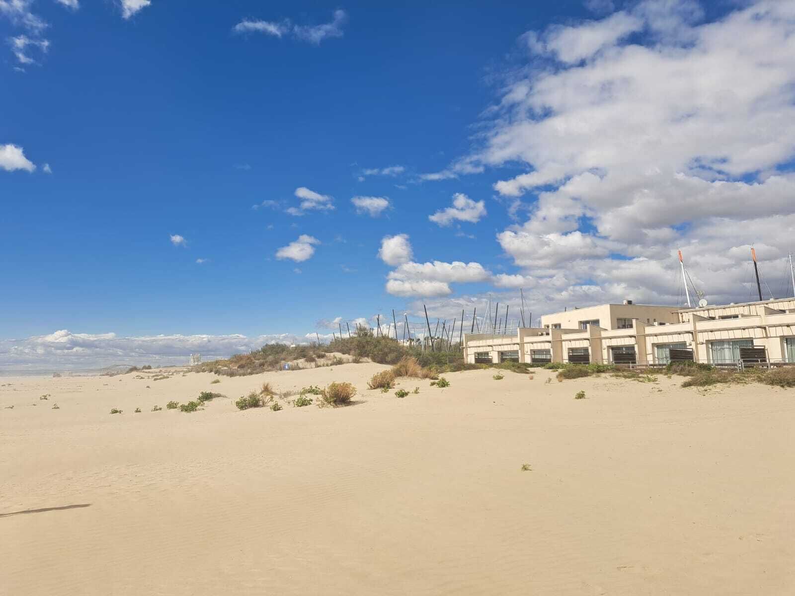 Een gebouw aan de kust met meerdere kamers, een zandstrand voorop en een heldere lucht met enkele wolken.