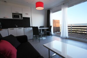 A modern kitchen with white cabinets, a microwave, and a dining area with a table and chairs. - Residence Côté Mer (La Grande-Motte)