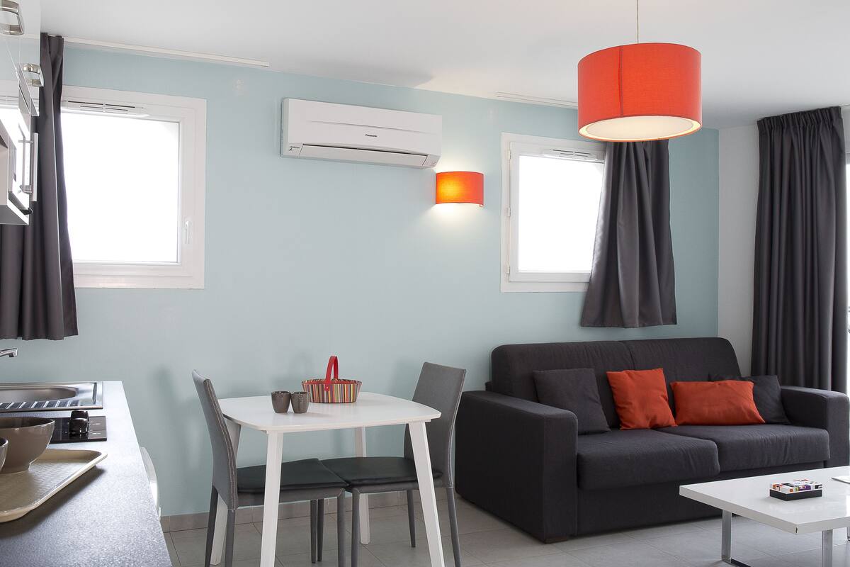 Ein modernes Wohnzimmer mit einer Couch, einem Esstisch und einer Küchenzeile mit Spüle und Schränken.