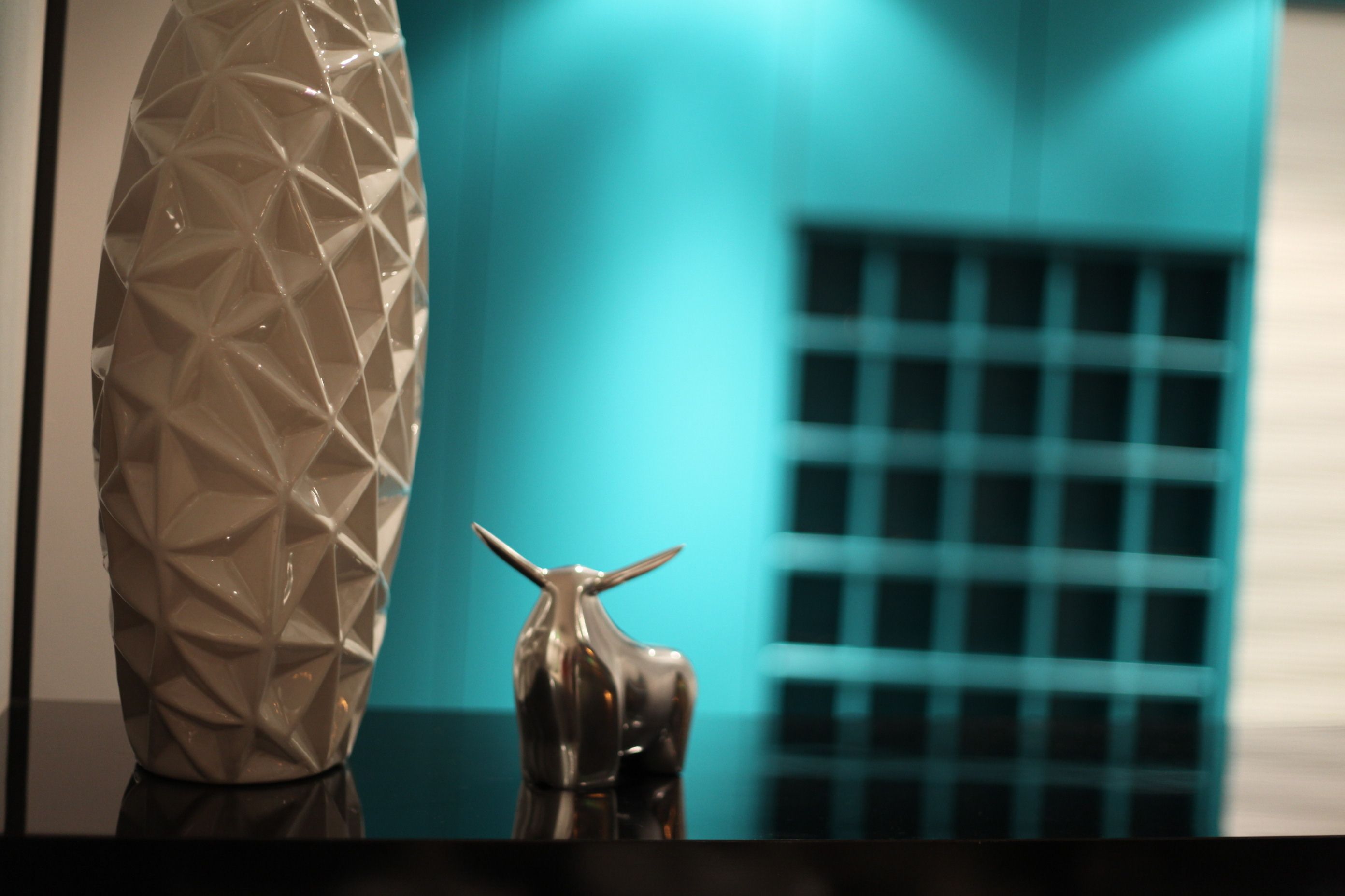 Een modern interieur met een geometrische vaas en een metalen sculptuur op een reflecterend oppervlak.