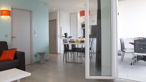 A modern living room with a sofa, a coffee table, and a dining area with a table and chairs. - Residence Côté Mer (La Grande-Motte)