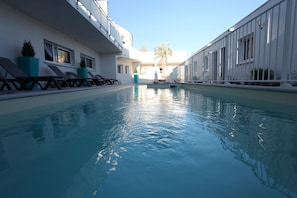 A swimming pool with lounge chairs and potted plants, surrounded by a white building with large windows. - Residence Côté Mer (La Grande-Motte)