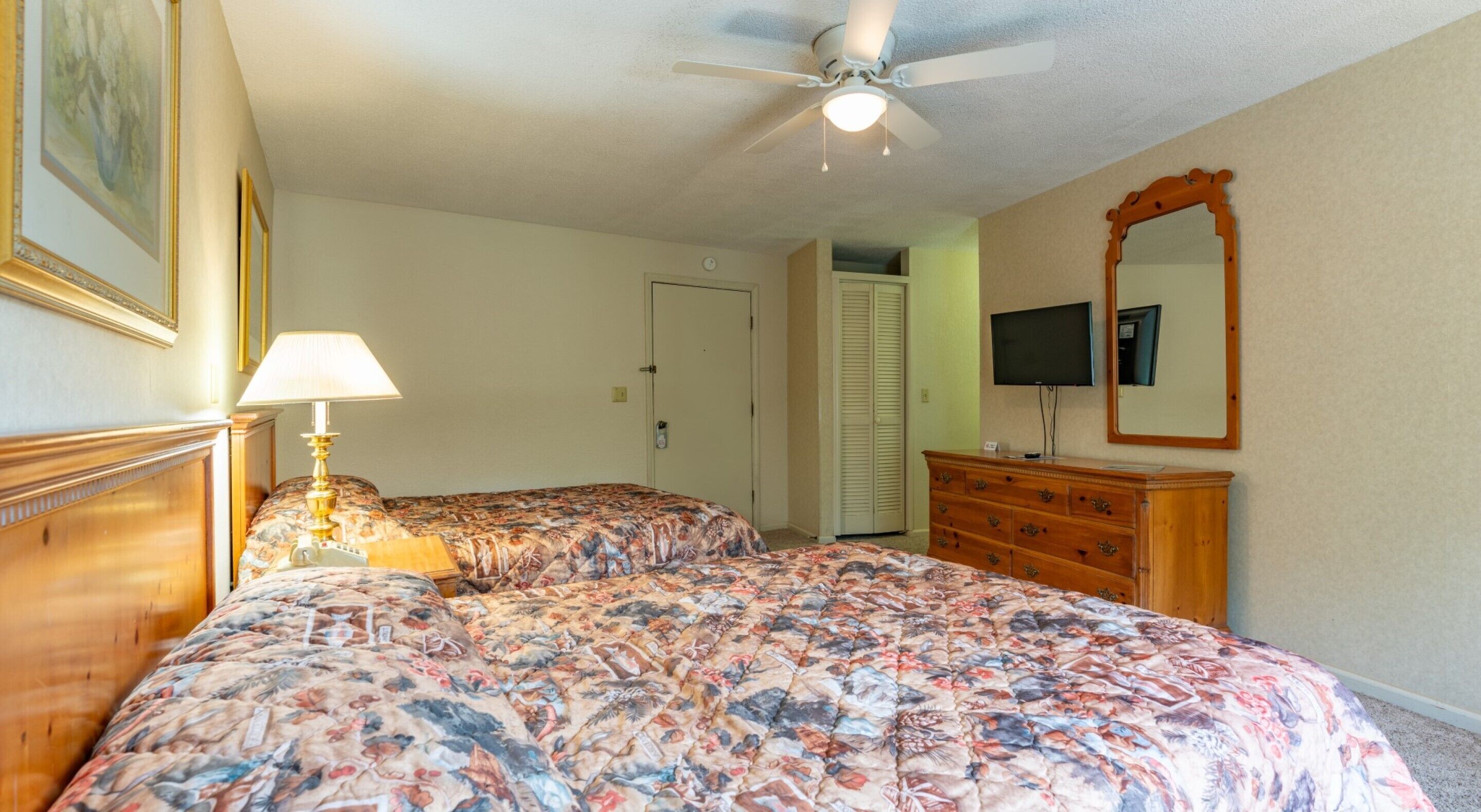 Un dormitorio con dos camas, ventilador de techo, televisión, cómoda y espejo.
