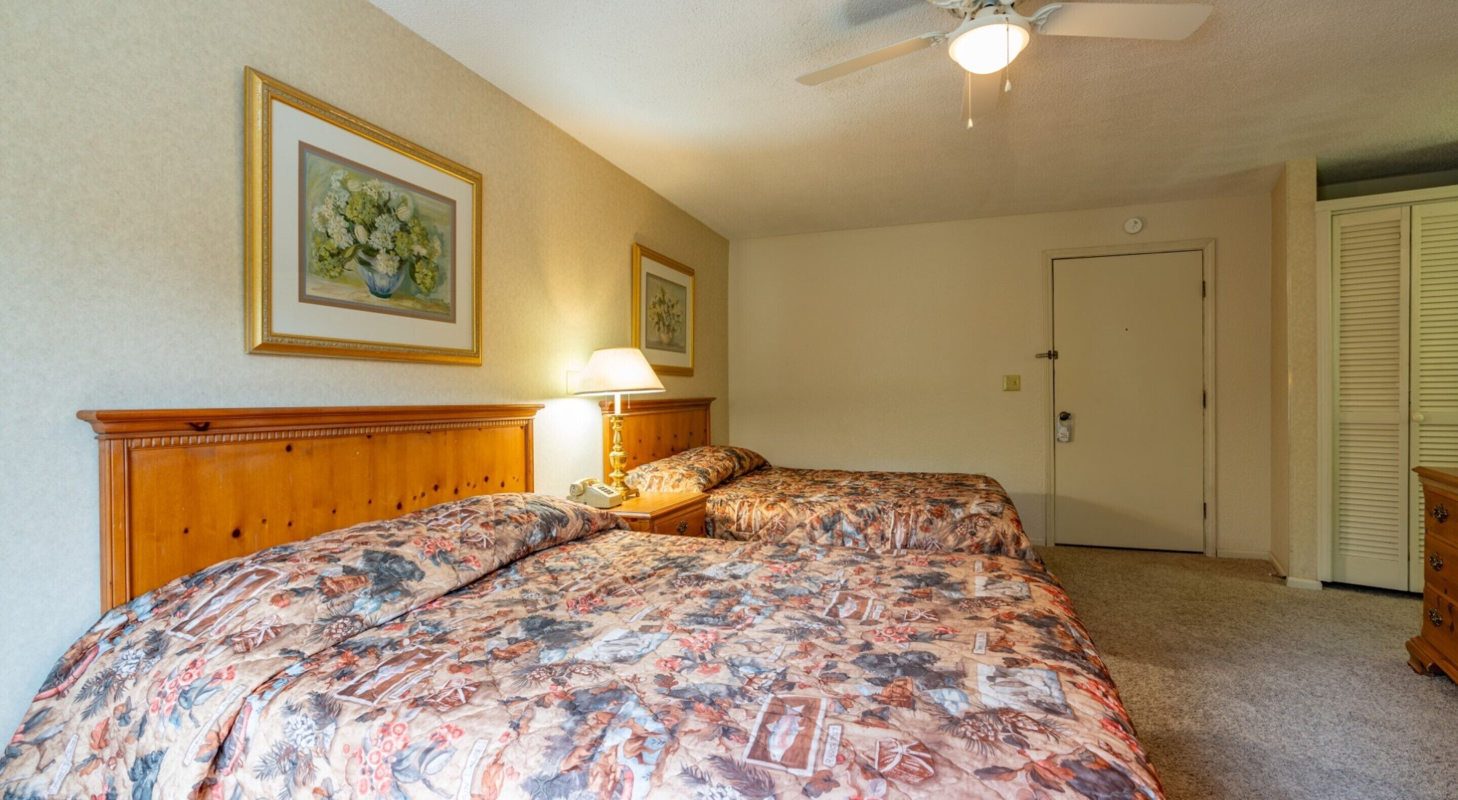 A bedroom with two beds, a ceiling fan, and a door.