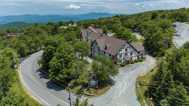 A large, two-story house with a steeply pitched roof, surrounded by lush greenery and a winding road. - 4 Seasons at Beech Mountain (Banner Elk)