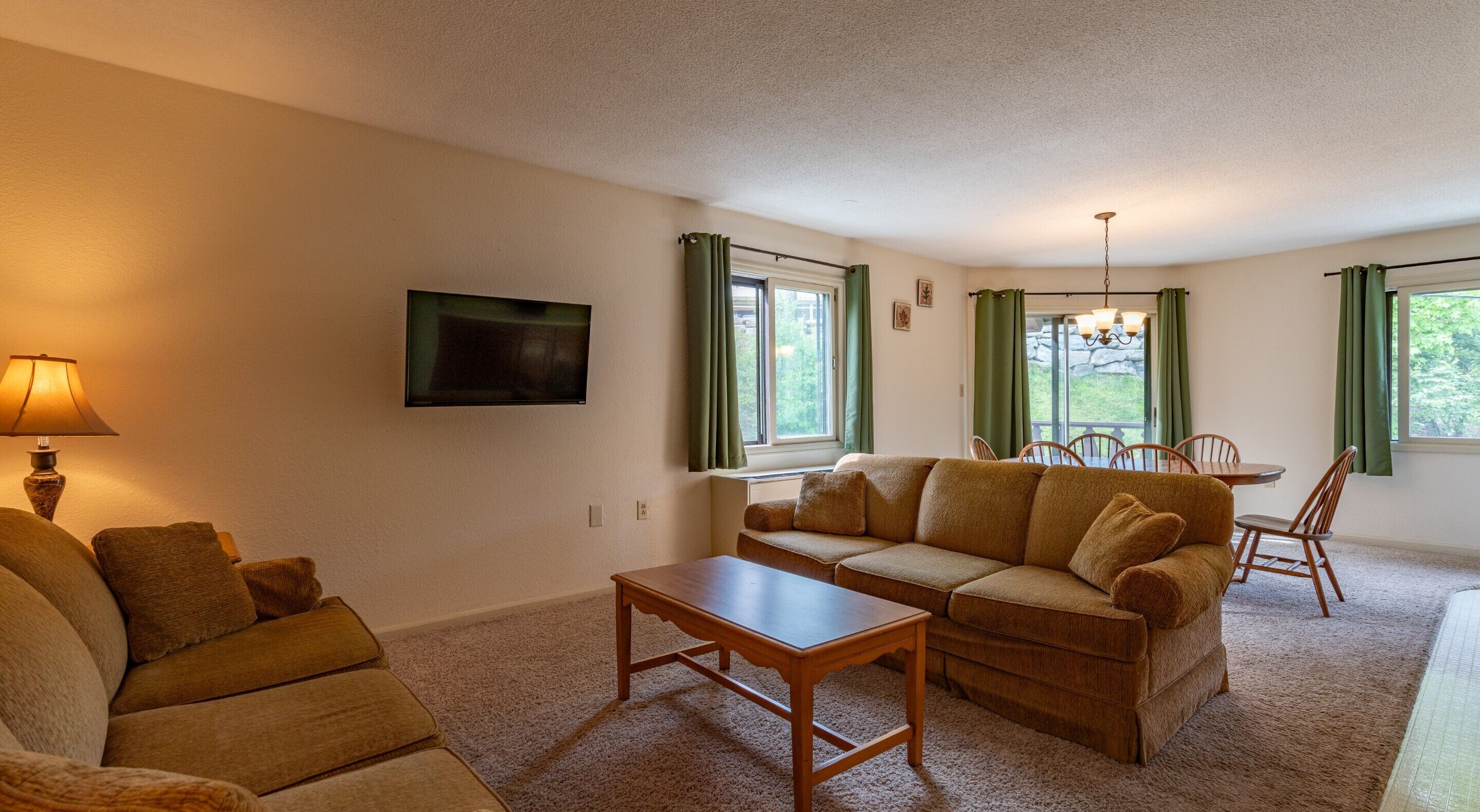 A cozy living room with a sofa, a coffee table, and a TV mounted on the wall.