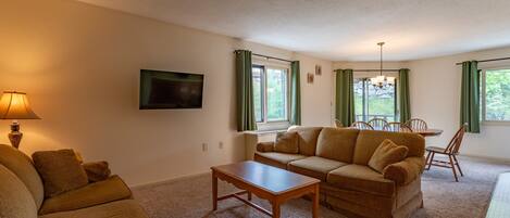 A cozy living room with a sofa, a coffee table, and a TV mounted on the wall.