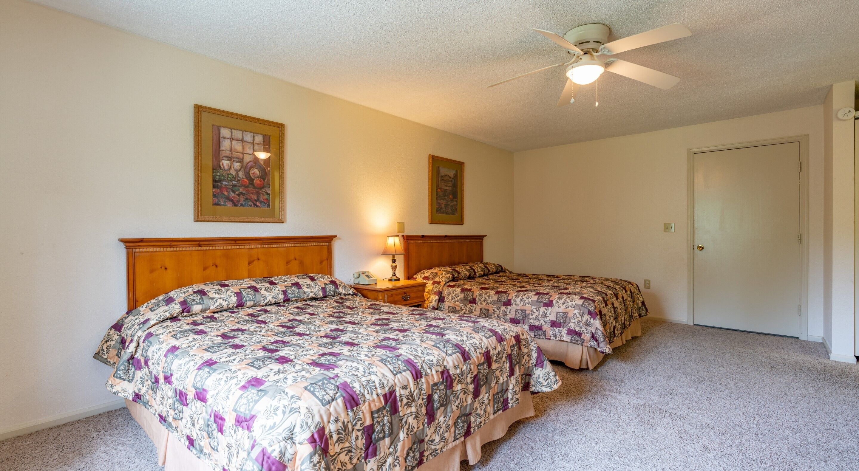 A bedroom with two beds, a ceiling fan, and two wall-mounted lamps.