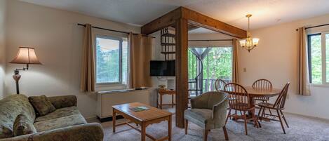 A living room with a sofa, coffee table, TV, and a dining area with chairs and a table.