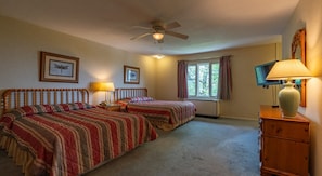 A bedroom with two beds, a ceiling fan, a window with curtains, and a lamp on a dresser.