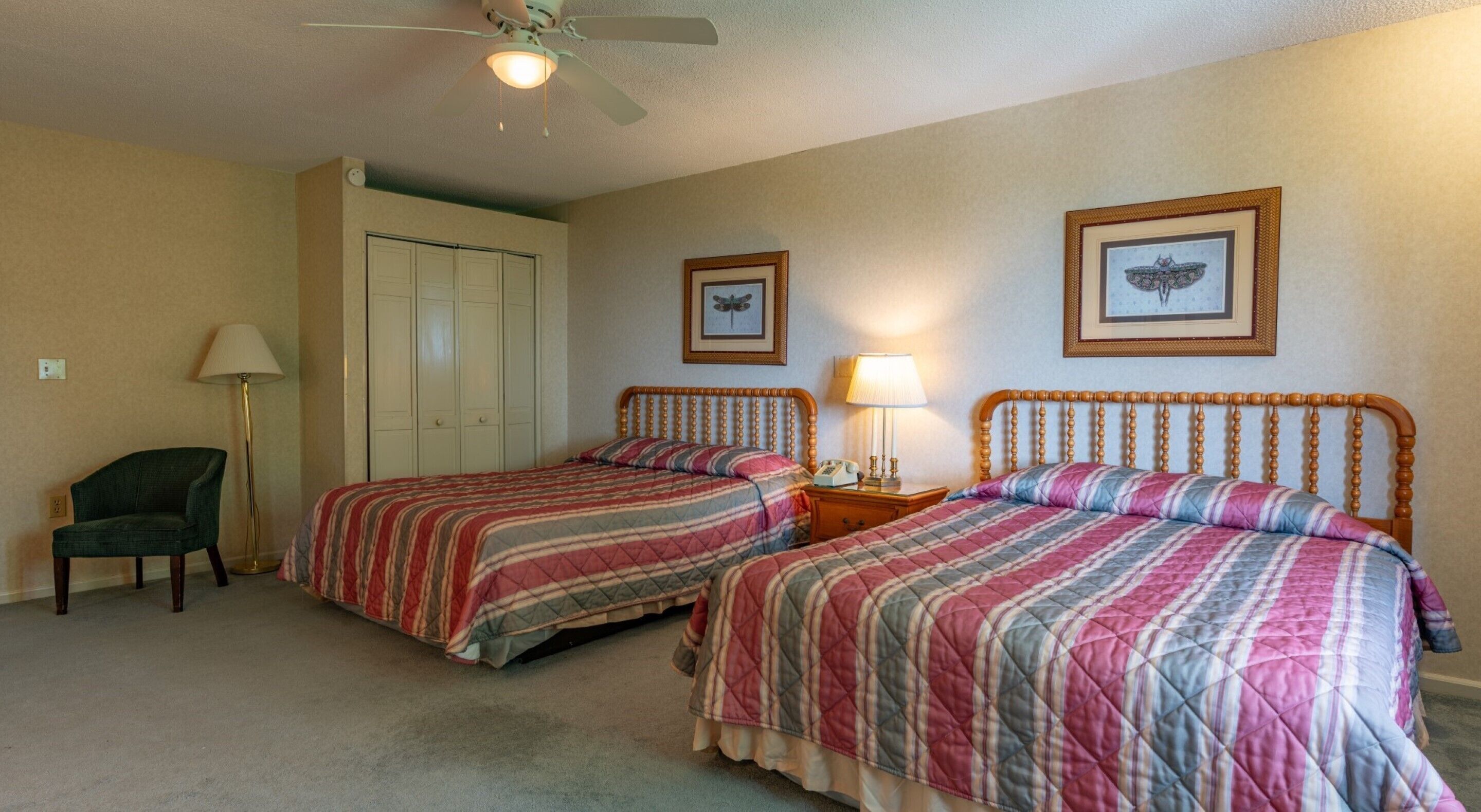 A bedroom with two beds, a chair, a floor lamp, and a ceiling fan.