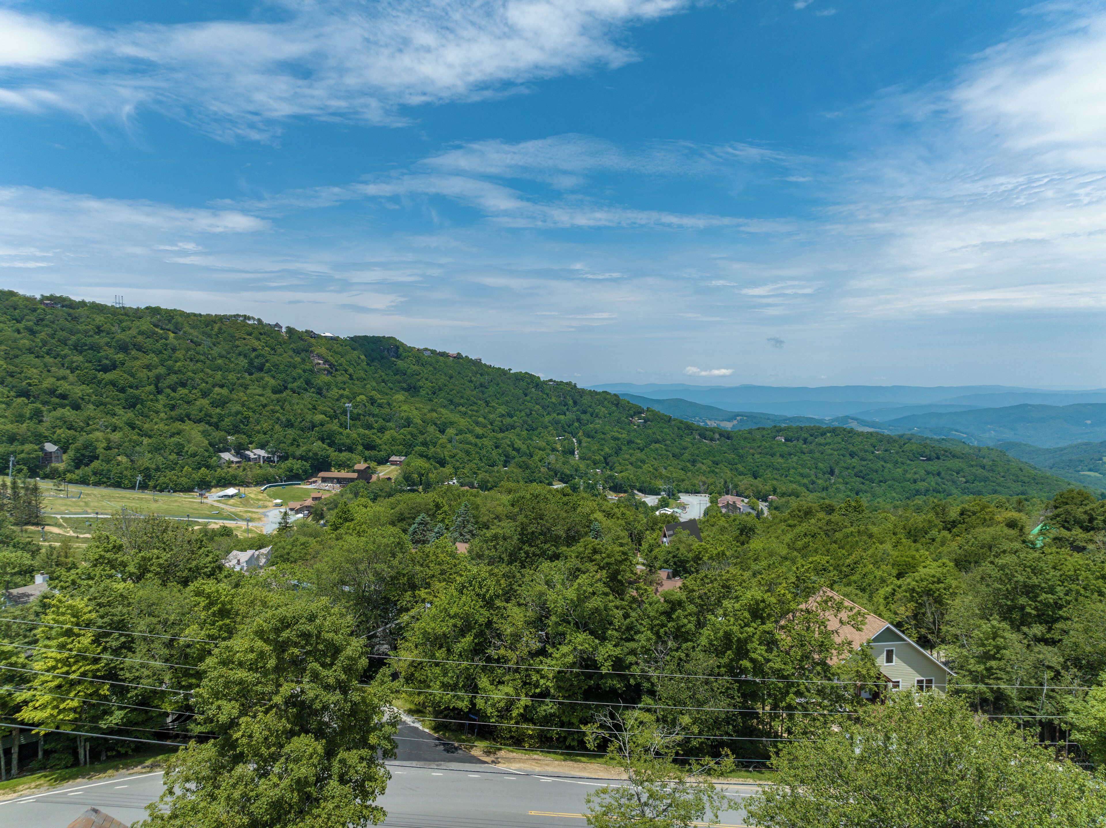A residential area with houses surrounded by dense green forest and hills in the background.