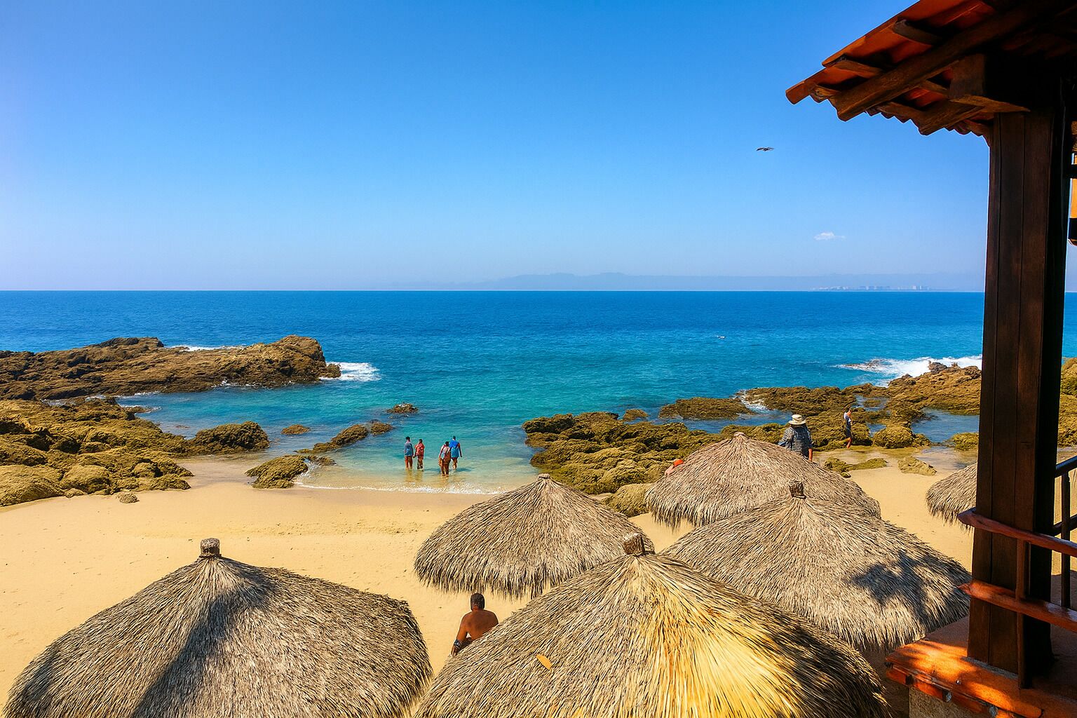 Una playa con sombrillas de paja, costa rocosa y mar azul cristalino.