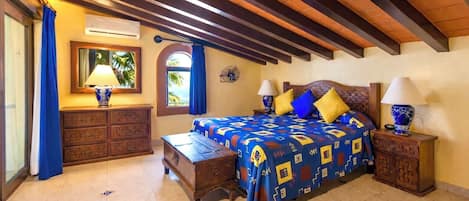 Un dormitorio con cama, dos mesitas de noche, cómoda, ventilador de techo y ventana con cortinas.