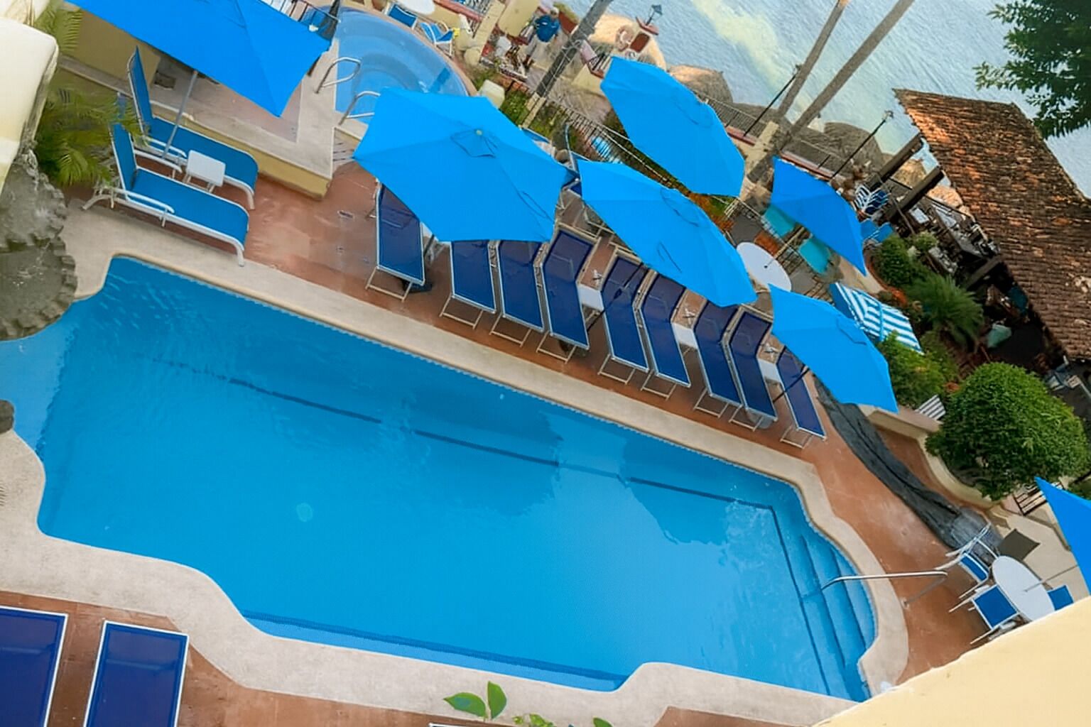 A swimming pool with blue umbrellas and lounge chairs.