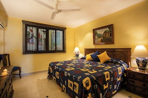 A bedroom with a bed, two bedside lamps, a ceiling fan, a window with blinds, and a painting on the wall. - Lindo Mar Resort (Puerto Vallarta)