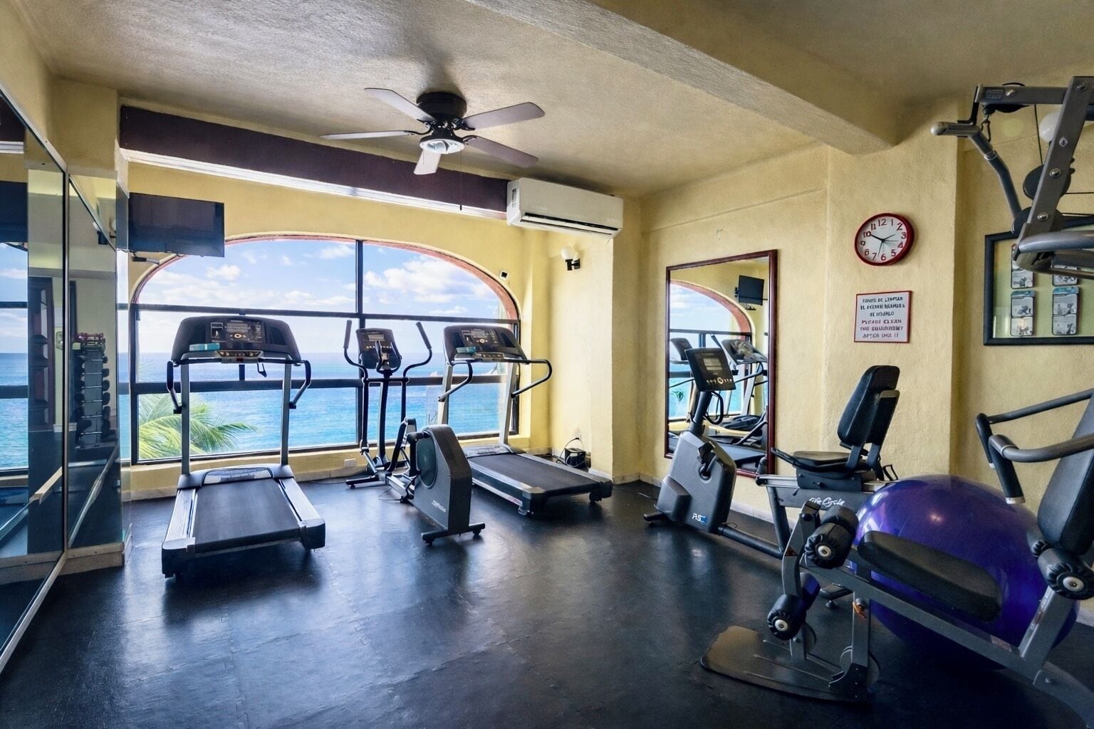 Un gimnasio con cintas de correr, elípticas y una máquina de remo, con vista al océano.