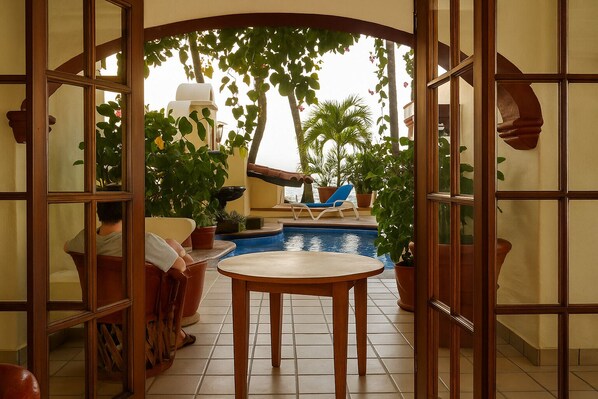 Zona de piscina con mesa y sillas, rodeada de plantas en macetas y vista al mar.