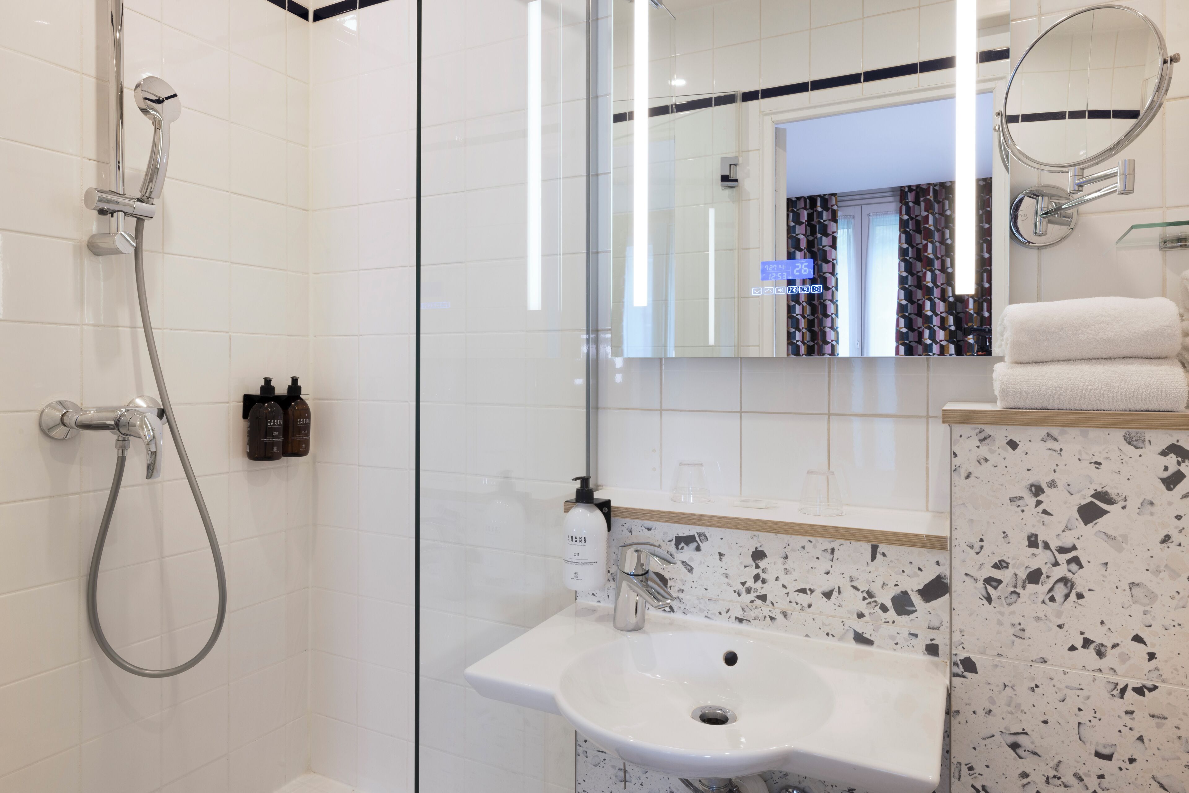 A modern bathroom with a glass shower enclosure, a white sink with a speckled backsplash, and a mirror with a round frame.