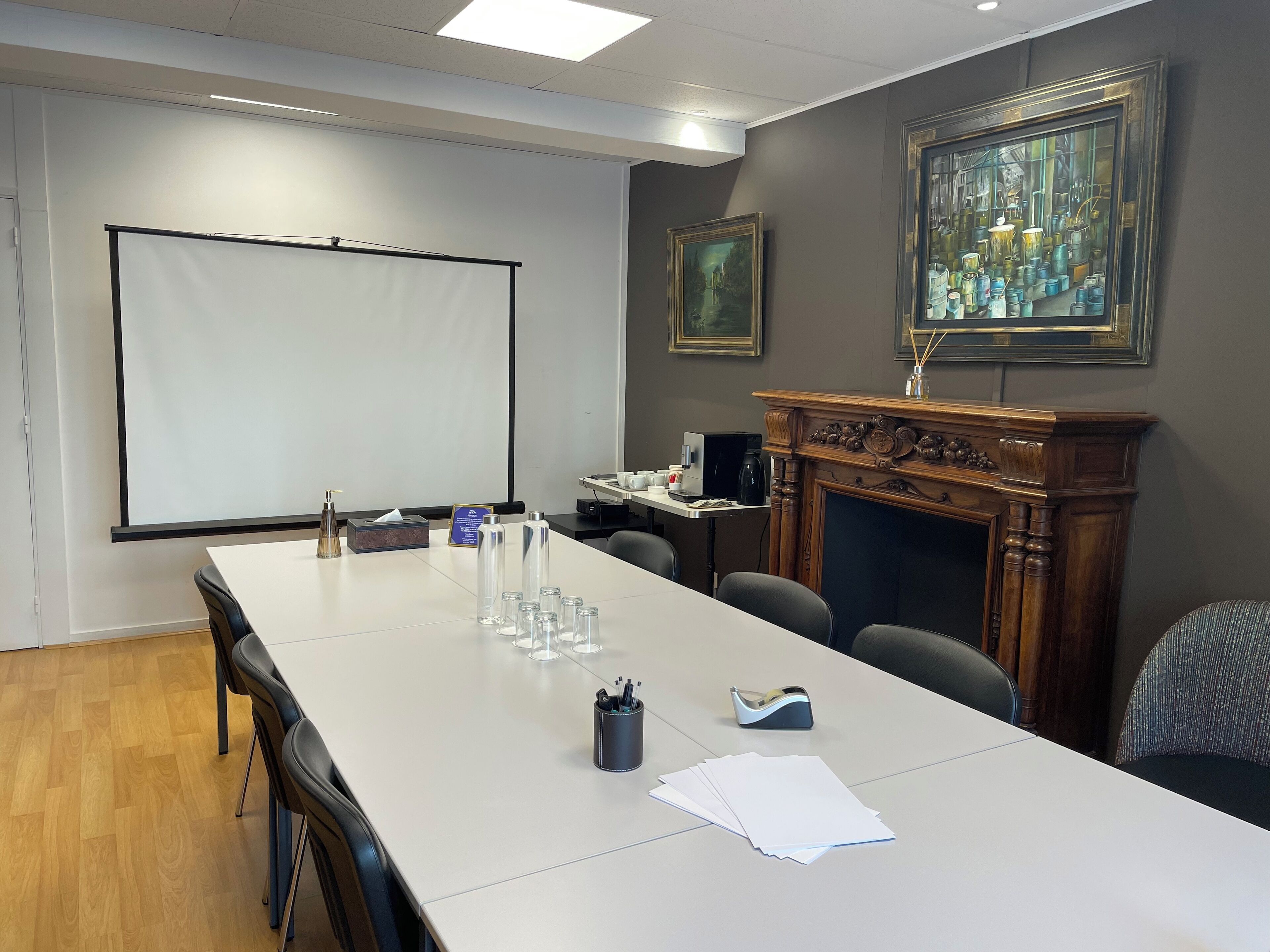 A conference room with a long table, chairs, a projector screen, a fireplace, and framed artwork on the wall.