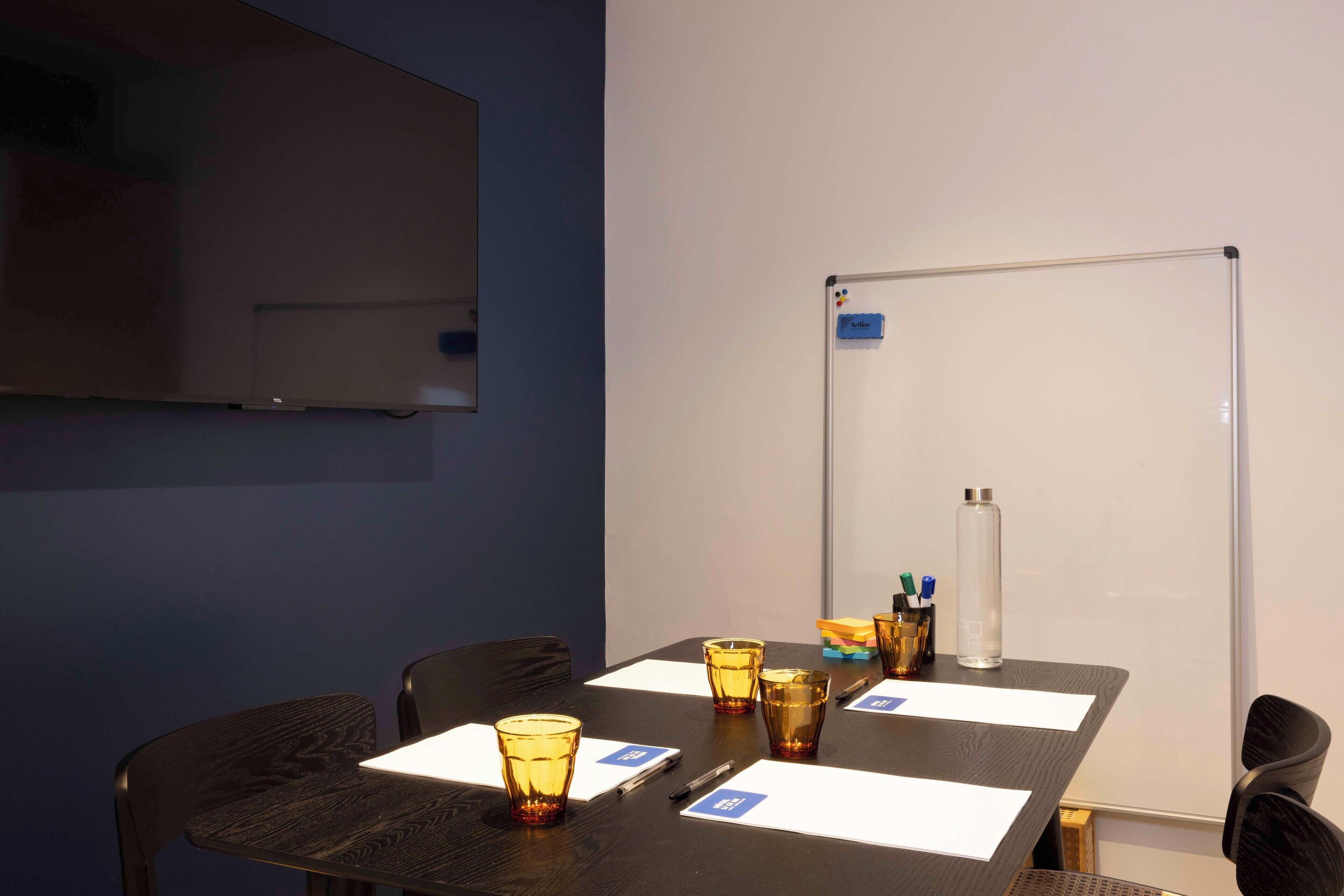 Une salle de conférence équipée d’un tableau blanc, d’un écran de projection et d’une table sur laquelle sont disposés des porte-noms et des verres.