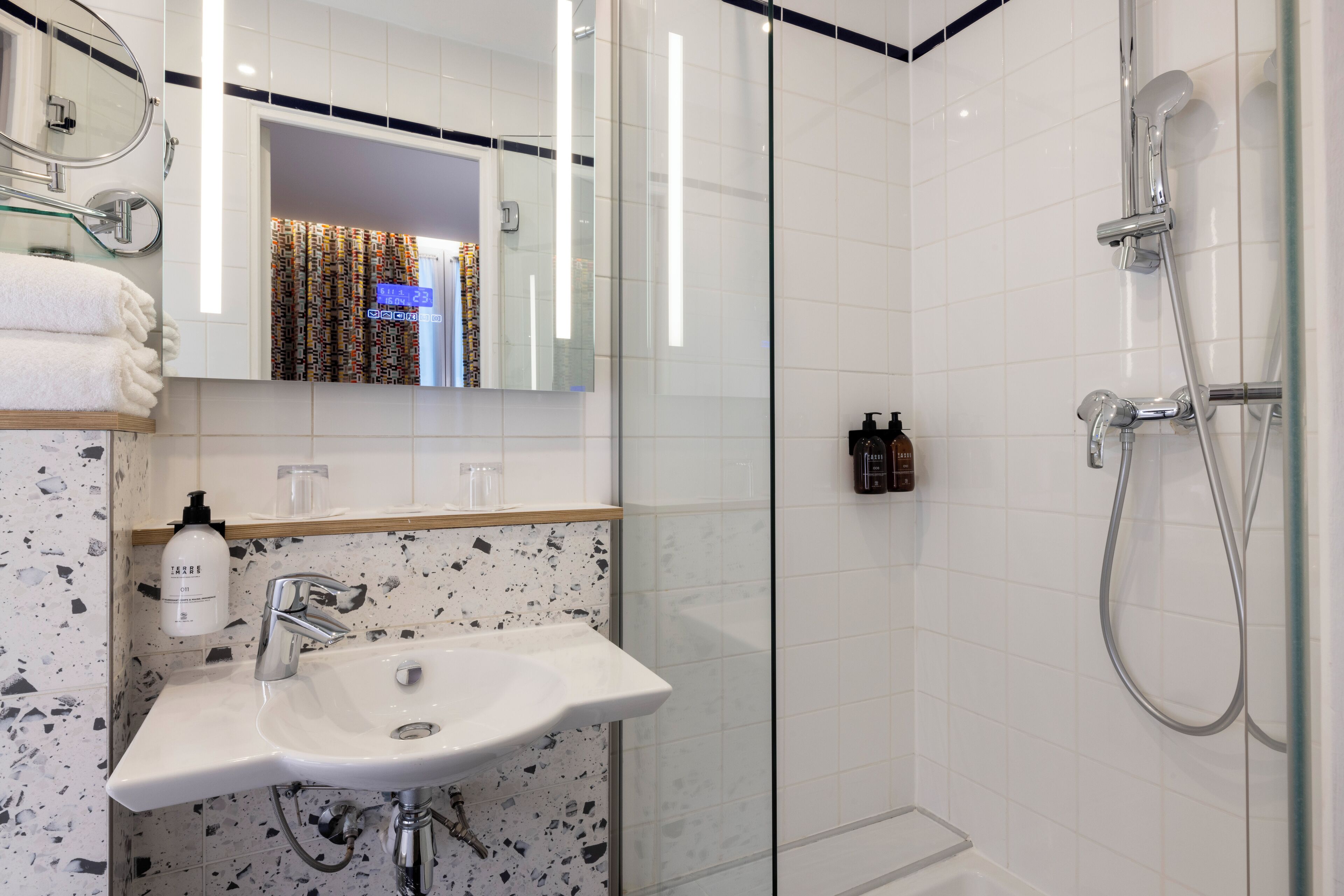 Un baño moderno con cabina de ducha de vidrio, un lavamanos blanco y un salpicadero de mármol, y un espejo sobre el lavamanos.