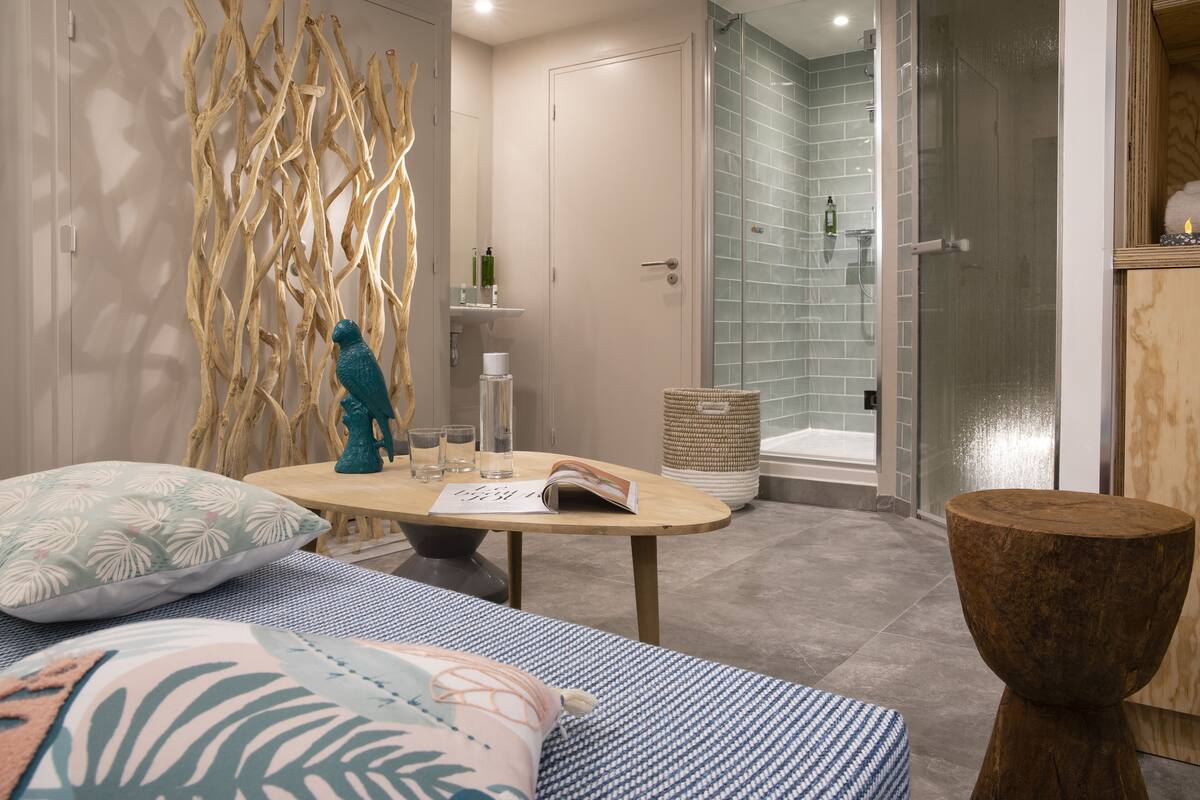 A modern bathroom with a glass shower, a wooden sculpture, and a small table with a book and glasses.