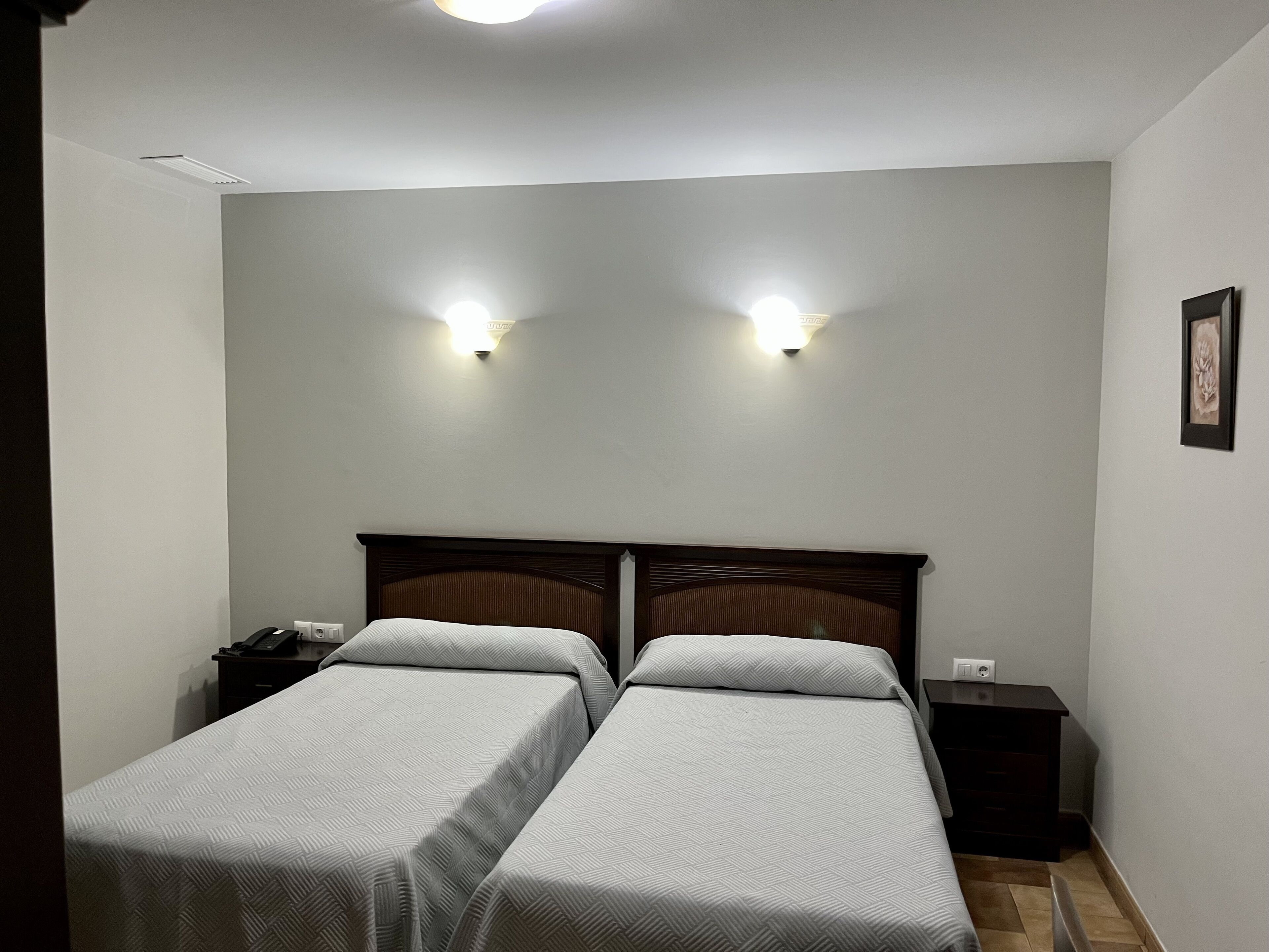 Un dormitorio con dos camas individuales, una mesita de noche con lámpara y una lámpara de pared.