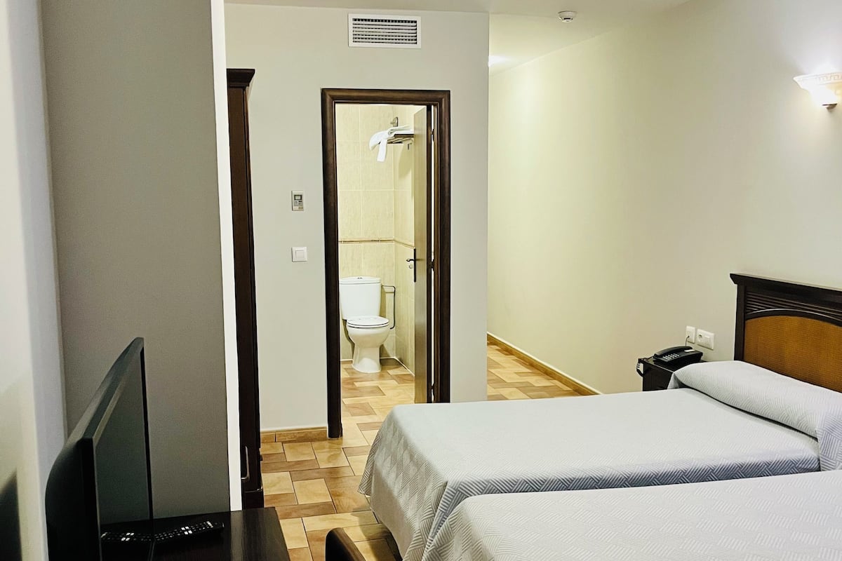 A hotel room with a desk, two beds, a television, and a bathroom visible through an open door.
