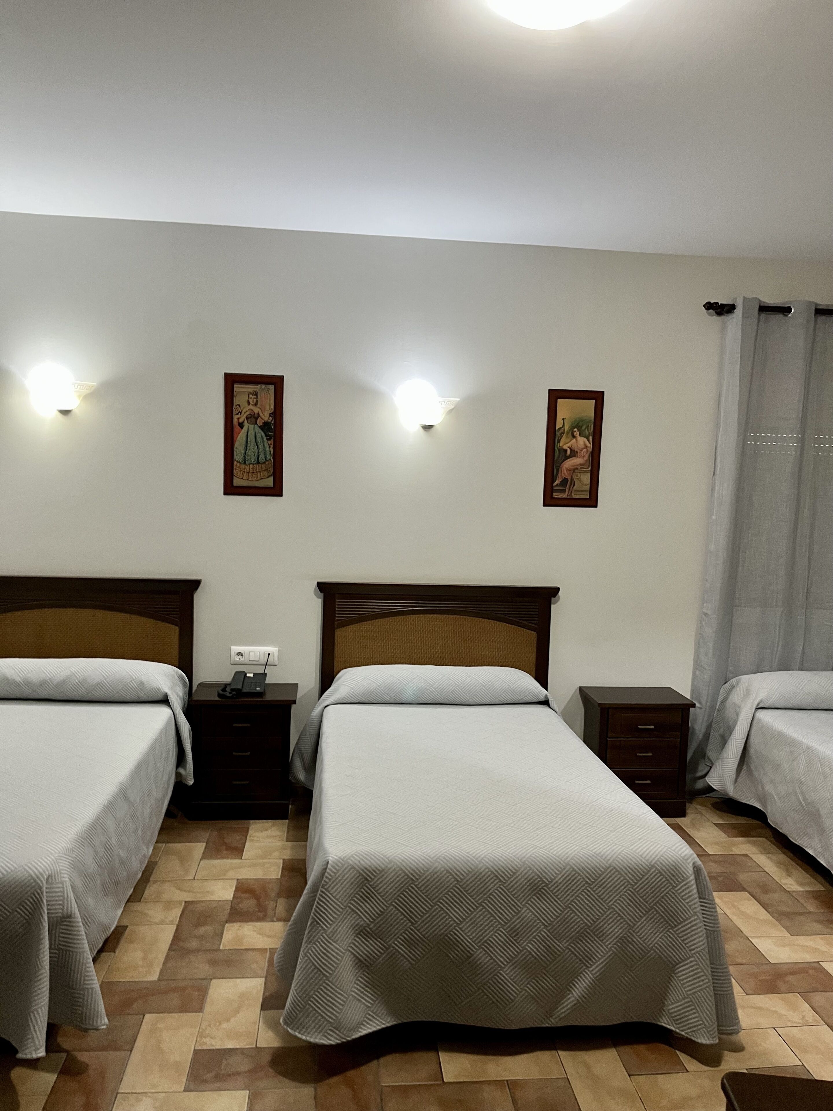 A hotel room with two single beds, a nightstand with a phone, and two wall-mounted light fixtures.