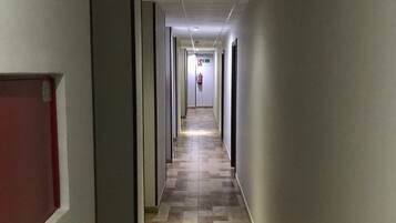 Un pasillo largo y estrecho con suelo de baldosas y puertas a ambos lados.