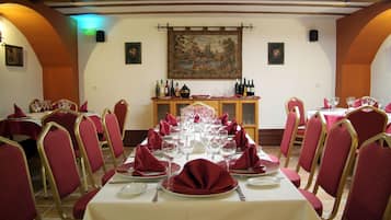 Comedor con mesas dispuestas para una comida, sillas tapizadas en rojo y una decoración de cuadros en la pared.