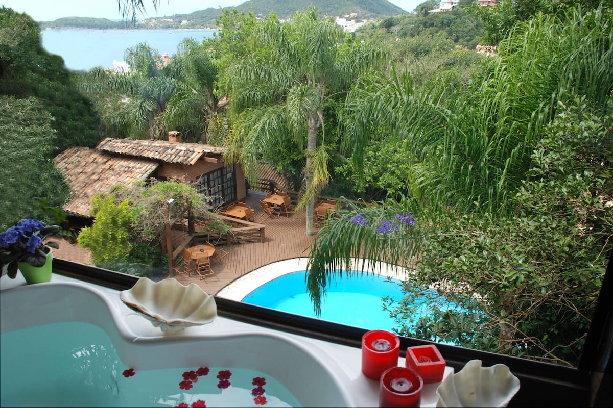 Une piscine entourée d’une végétation luxuriante, avec une terrasse en bois et un bâtiment rustique doté d’un toit de chaume.