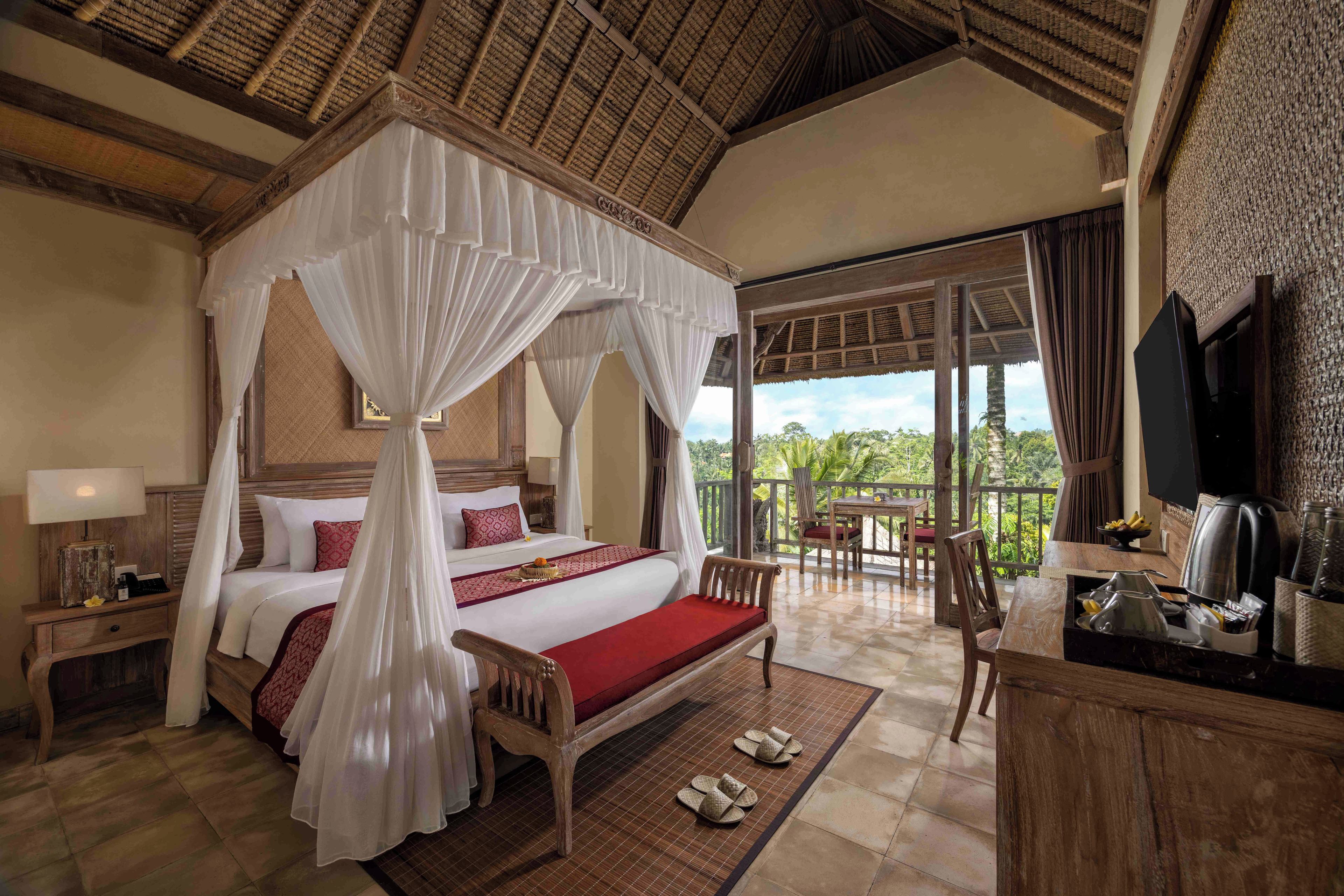 A four-poster bed with a canopy, a wooden desk with a chair, a table with chairs, and a view of the outdoors.
