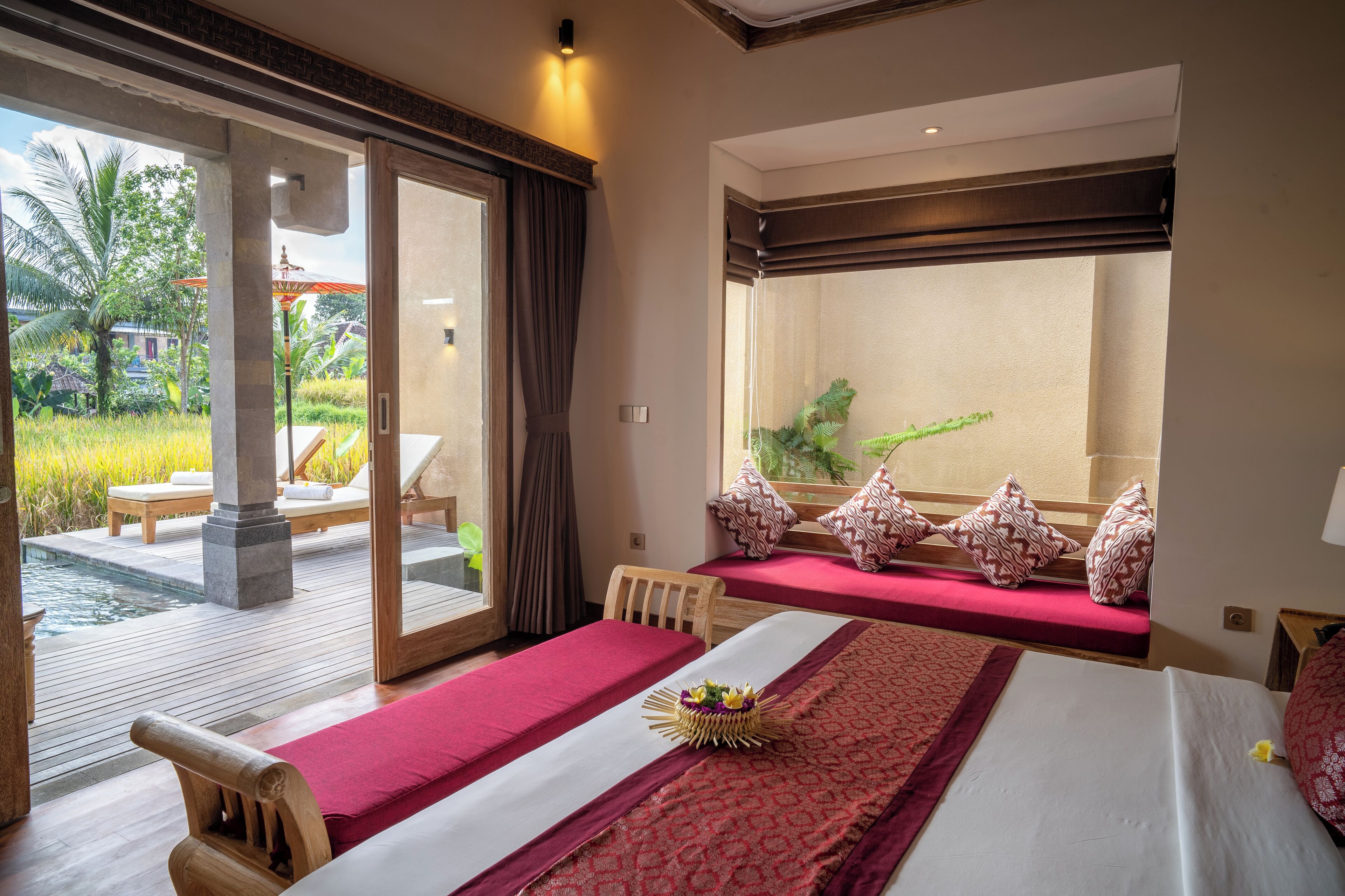 Habitación de hotel con una cama grande, una cama más pequeña, vista a un jardín y un balcón con piscina.