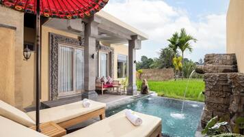 Zona de piscina con sillones de descanso, una mesa y un parasol decorativo.