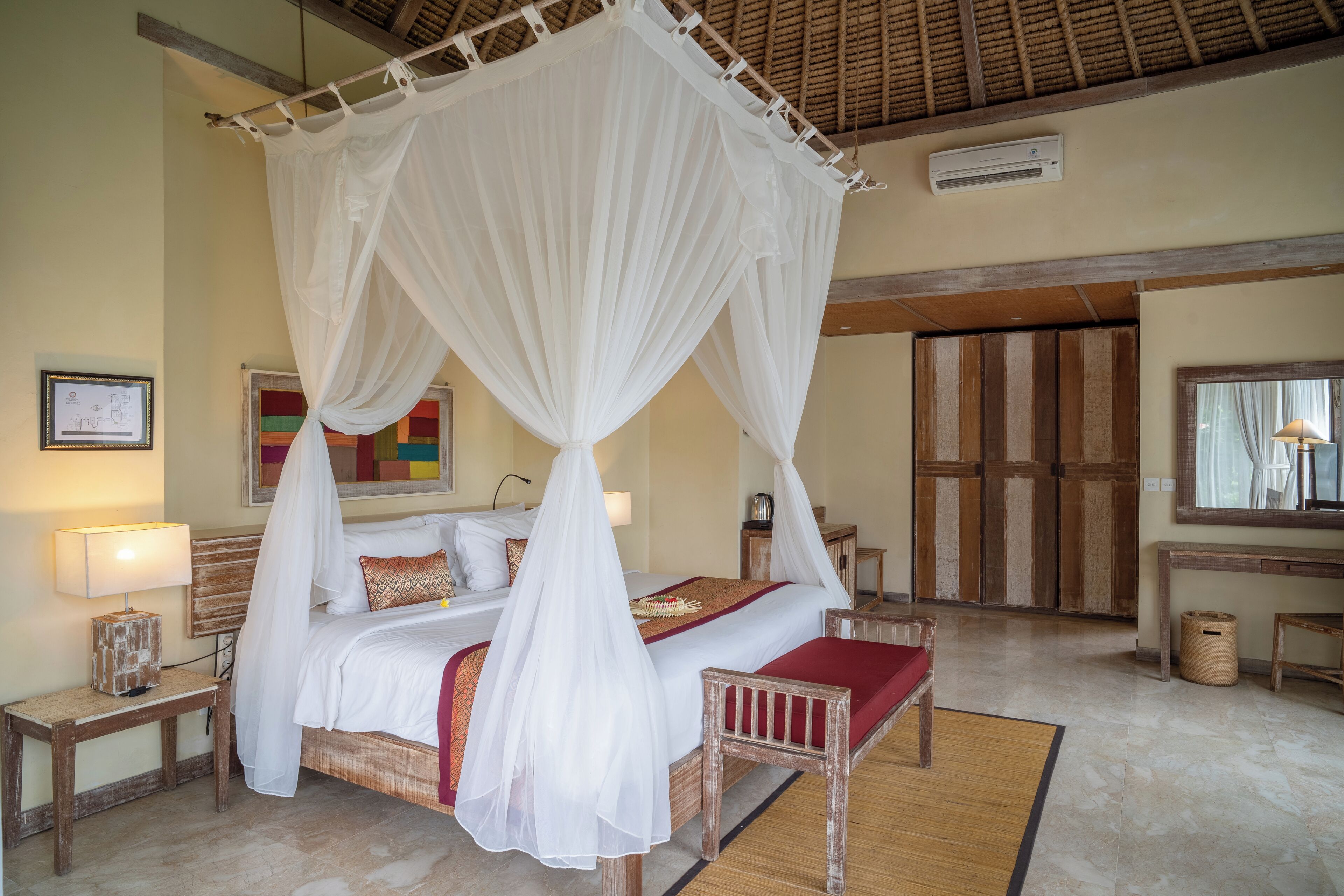 A bedroom with a four-poster bed, a bedside table with a lamp, a wooden bench, and a large mirror.