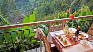 Ein Balkon mit Esstisch, umgeben von üppiger Vegetation und Blick auf ein Tal.