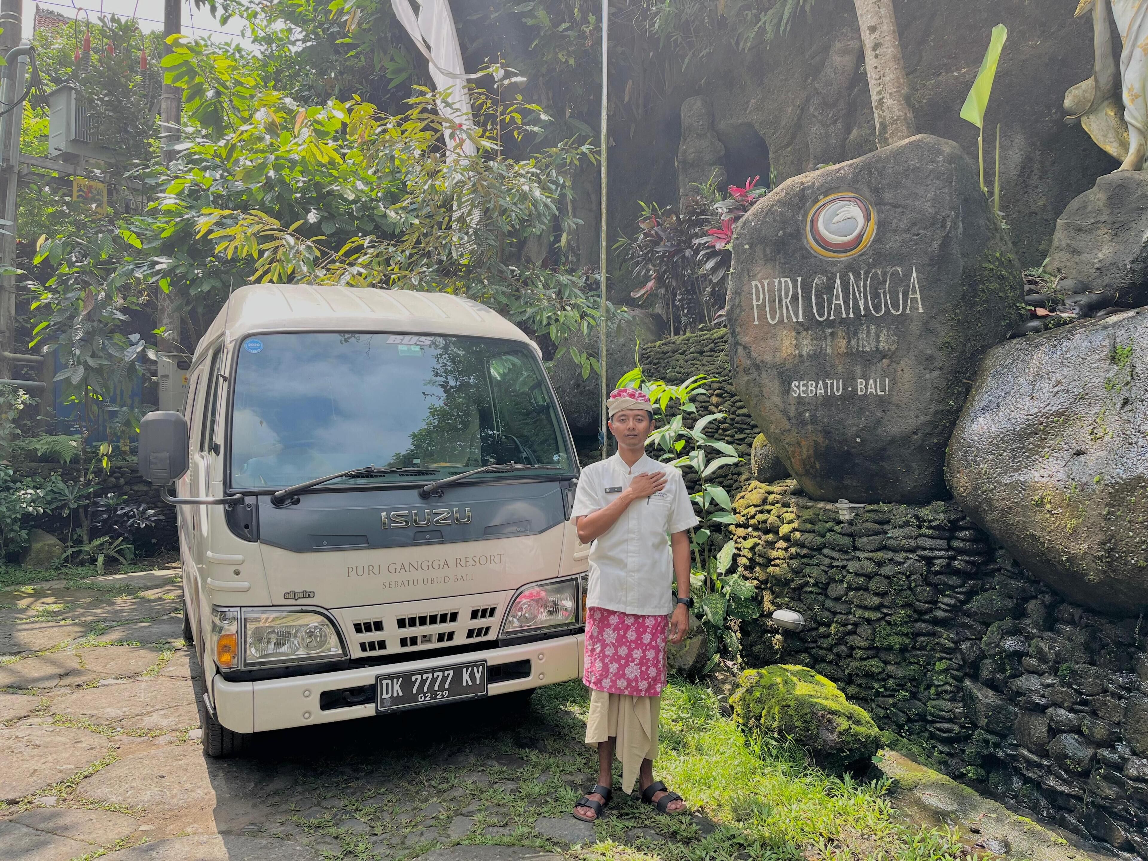 Una camioneta blanca Isuzu estacionada frente a un muro de piedra con un letrero que dice "Puri Gangga Resort" y "Sebatu Ubud Bali".