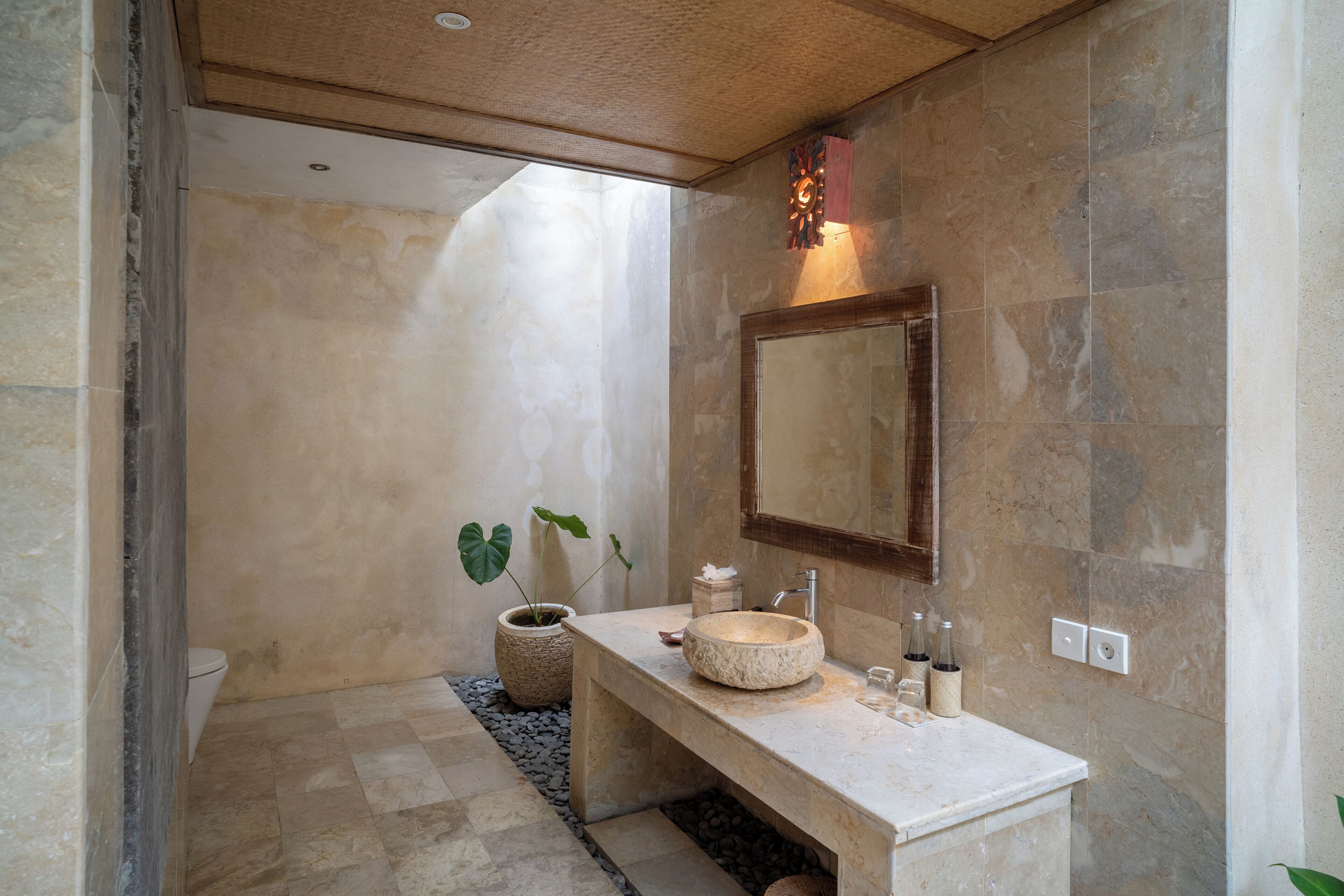 Une salle de bain avec un lavabo en pierre, un miroir et une plante en pot.