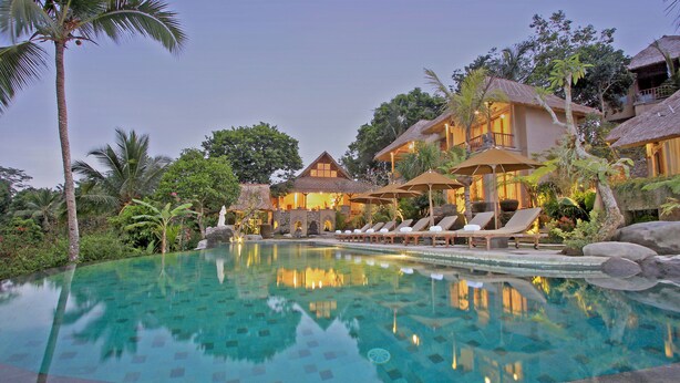Ein Resort mit Swimmingpool, Liegestühlen und strohgedeckten Gebäuden.
