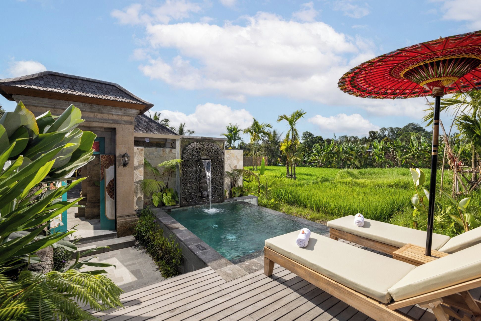 A pool area with a waterfall feature, lounge chairs, and a red umbrella.