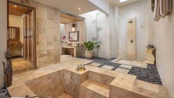 Un baño moderno con una bañera grande, un lavamanos y una zona de ducha. Hay un tragaluz sobre la bañera y una planta en maceta cerca del lavamanos.