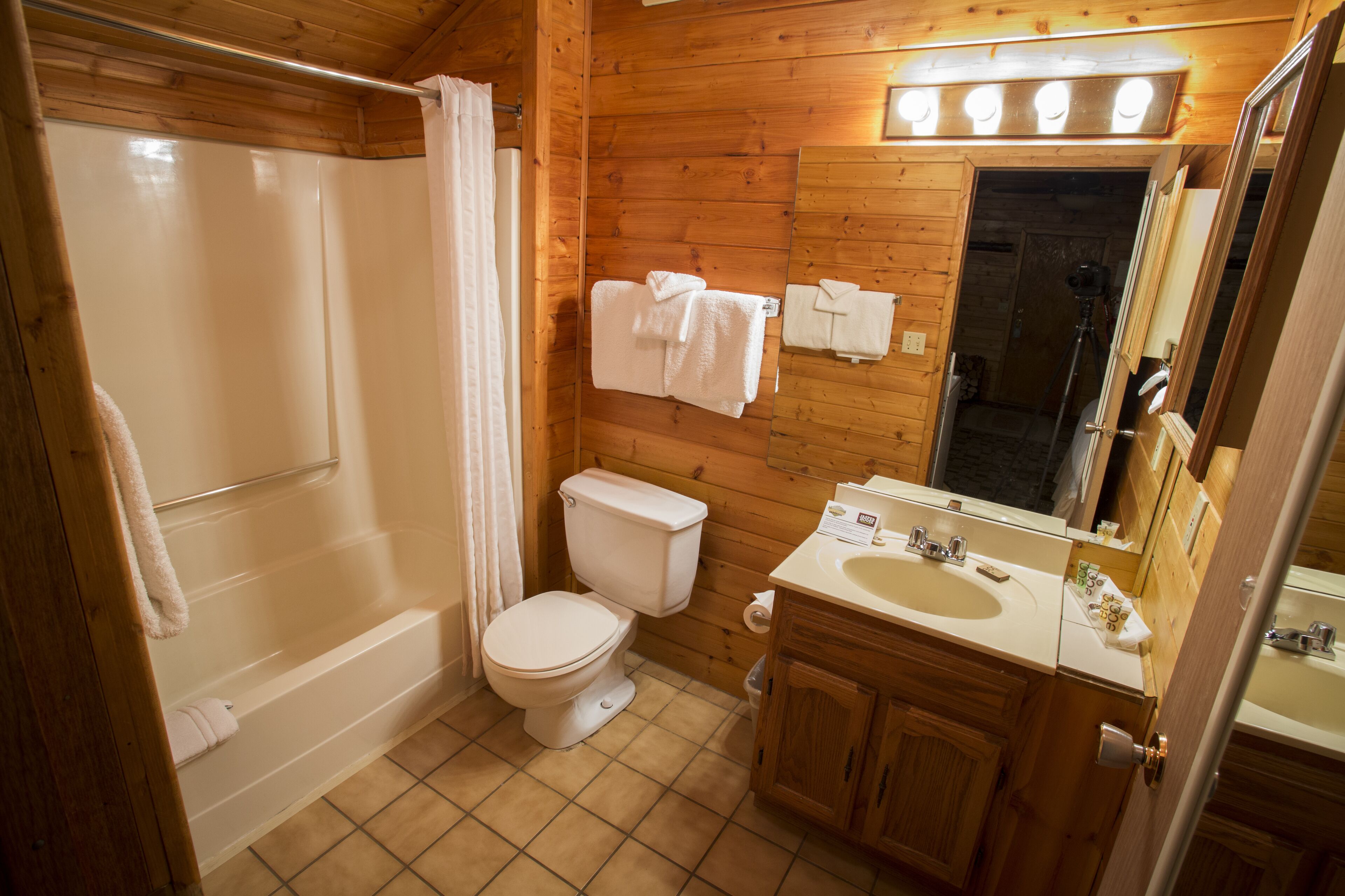 A wooden cabin bathroom with a bathtub, toilet, and sink.